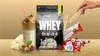 A collection of protein powder, candies, and a drink, arranged on a golden background. Produktbild-Vorschau