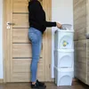 A person is shown sorting trash into a stack of white bins. Voir les images du produit