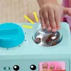 A child's hand is interacting with a toy coffee maker, specifically turning a dial and looking into a clear compartment containing coffee beans. Náhľad obrázku produktu