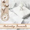 A stack of white muslin cloths with a small white bunny toy on top, set against a rumpled white fabric background. A decorative banner with text is at the bottom, and a graphic of cotton bolls is on the left. Produktbild-Vorschau