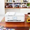 A white Canon PIXMA TS9551Ca printer is placed on a wooden table, with a bookshelf in the background. Podgląd zdjęcia produktu