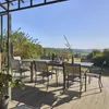 An outdoor dining set on a wooden deck with a scenic view of rolling hills and trees under a clear blue sky. Anteprima dell’immagine prodotto