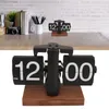 A close-up shot of a black flip clock on a wooden base, set against a white brick wall background. Náhled obrázku produktu