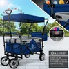 A blue foldable wagon with a canopy is shown outdoors with a Ferris wheel in the background. Produktbild-Vorschau