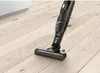 A black cordless vacuum cleaner is shown on a light-colored wooden floor, with a hint of white cabinetry in the background. Voir les images du produit