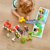 A child playing with LEGO DUPLO fire truck toys on a wooden floor, with an instruction booklet nearby. Produktbild-Vorschau