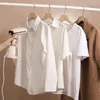 A hand holds a beige and pink handheld steamer near white shirts hanging on a rack, with a brown coat on the far right. Produktbild-Vorschau