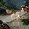 A set of LED tea lights on a charging base, surrounded by Christmas decorations like pine branches and ornaments. Produktbild-Vorschau