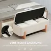 A cream-colored storage bench with its lid open, revealing pillows inside, placed next to a bed. Voir les images du produit