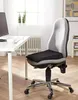 A black orthopedic seat cushion is placed on a gray office chair next to a white desk with a computer monitor and a cup of coffee. Produktbild-Vorschau