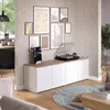 A living room scene featuring a white sideboard with a wooden top, a record player, and framed artwork on the wall. Náhled obrázku produktu