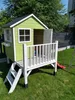 A wooden playhouse with a porch and slide in a backyard setting. Produktbild-Vorschau
