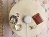 A Google Nest Mini is placed on a round wooden table next to a succulent plant, a glass of water, a wallet, and keys. Produktbild-Vorschau