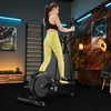 A woman is exercising on a crosstrainer in a home gym setting. Produktbild-Vorschau
