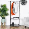 A black metal garment rack with clothes and shoes on it, next to a potted plant and a chair. Náhľad obrázku produktu