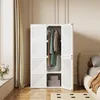 A white foldable wardrobe with clothes hanging inside, placed in a bedroom next to a bed and a window with curtains. Náhled obrázku produktu