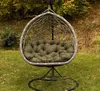 A hanging egg chair with a green cushion sits on a grassy lawn with autumn foliage in the background. Voir les images du produit