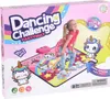 The image shows the packaging of a children's dancing challenge party mat with a unicorn theme. A young girl is posing on the mat, and cartoon unicorns are featured on the packaging and the mat itself. Produktbild-Vorschau