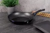 A frying pan is placed on a dark stone countertop, with a potted plant in the background. Podgląd zdjęcia produktu