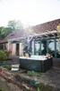 A couple relaxing in a hot tub on a patio next to a rustic building. Produktbild-Vorschau