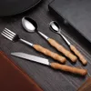 A set of four cutlery pieces with wooden handles is arranged on a dark wooden surface. Voir les images du produit