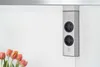 A corner power outlet unit mounted on a white wall, with a bouquet of tulips in the foreground. Voir les images du produit