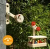 A wooden zipline system for toys, attached to a wooden post, with greenery in the background. Produktbild-Vorschau