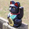 A black Maneki-neko (lucky cat) figurine sits on a wooden post outdoors. Produktbild-Vorschau