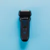 A black electric shaver with blue accents is placed on a light blue background. Anteprima dell’immagine prodotto