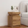 A wooden nightstand with two drawers and a small plant and framed picture on top, next to a bed. Podgląd zdjęcia produktu