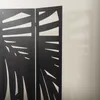 A close-up view of a black, 3-panel room divider with a cut-out pattern, casting a shadow on a light-colored wall. Náhled obrázku produktu