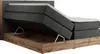 A king-size boxspring bed with its storage compartment open, revealing the interior and a lifting mechanism. The bed is upholstered in dark gray fabric and features a wooden frame base in a Wotan Oak finish. Produktbild-Vorschau