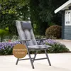A garden chair with a striped cushion and headrest is placed outdoors on a patio, surrounded by purple flowers and greenery, with a small wooden shed in the background. Produktbild-Vorschau