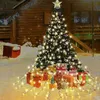 A decorated Christmas tree with presents underneath, set against a wooden cabin in a snowy environment. Produktbild-Vorschau