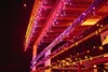 Icicle lights in various colors are draped along the eaves and railings of a wooden building at night. Náhled obrázku produktu
