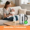 A mother is holding a baby on a couch, with a baby bottle and a kettle on a coffee table in the foreground. Produktbild-Vorschau