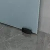 A close-up view of the bottom corner of a glass sliding door with a black door stop on a marble floor. Produktbild-Vorschau