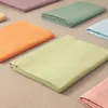 Several folded fabric sheets in various pastel colors are laid out on a textured surface. Produktbild-Vorschau