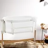A baby crib is shown in a room with a white wall and wooden floor. Produktbild-Vorschau