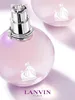 A close-up shot of a pink perfume bottle with a silver cap and a decorative emblem on the bottle. Another bottle is visible in the background. Podgląd zdjęcia produktu