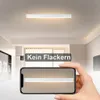 A hand holding a smartphone displaying a light fixture, with the actual light fixture visible on the ceiling above. Podgląd zdjęcia produktu