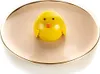 A yellow chick-shaped dessert on a light pink plate with a gold rim. Produktbild-Vorschau