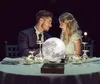 A couple having a romantic dinner outdoors at night, with a levitating moon lamp on the table. Produktbild-Vorschau