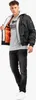A man wearing a black bomber jacket over a gray t-shirt and black jeans, posing against a white background. Produktbild-Vorschau