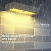 A modern outdoor wall light is shown mounted on a tiled wall during a rain shower. The light is illuminated, casting a warm glow. Produktbild-Vorschau