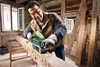 A man is sanding a large piece of wood with a belt sander in a rustic workshop. Produktbild-Vorschau