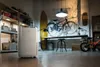 A De'Longhi dehumidifier is placed on a wooden floor in a garage or workshop setting, with bicycles, skateboards, and shelving in the background. Voir les images du produit
