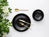 A flat lay of black plates, cutlery, and a bowl, with a sprig of white flowers and green leaves on the left. Náhľad obrázku produktu