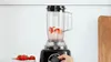 A blender with strawberries inside is being operated by a hand. Produktbild-Vorschau