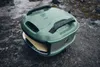 A green Gozney pizza oven sits on a wet, rocky surface, possibly outdoors. Produktbild-Vorschau
